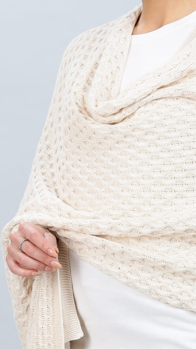 Person wearing a beige knitted shawl on a plain background